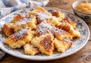 Fluffiger Kaiserschmarrn mit Skyr und Puderzucker auf einem blau-weißen Teller, daneben Apfelmus.