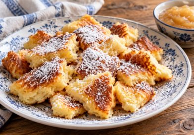 Fluffiger Kaiserschmarrn mit Skyr und Puderzucker auf einem blau-weißen Teller, daneben Apfelmus.