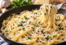 Parmesan-Spaghetti mit Knoblauchcreme, Petersilie und feinen Chiliflocken in einer Pfanne, auf einer Gabel aufgedreht.